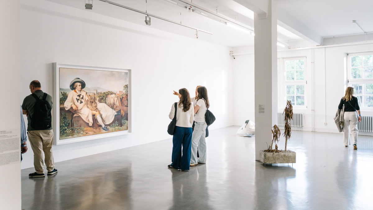 Mehrere Personen in einem Ausstellungsraum vor einem Gemälde und mehreren Skulpturen