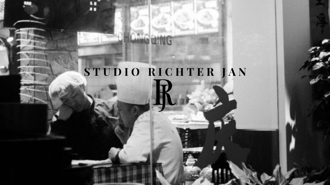 Schwarzweiß-Straßenfoto aus Chongqing: zwei Köche hinter Restaurantscheibe, Schriftzug Studio Richter Jan mit RJ-Monogramm.