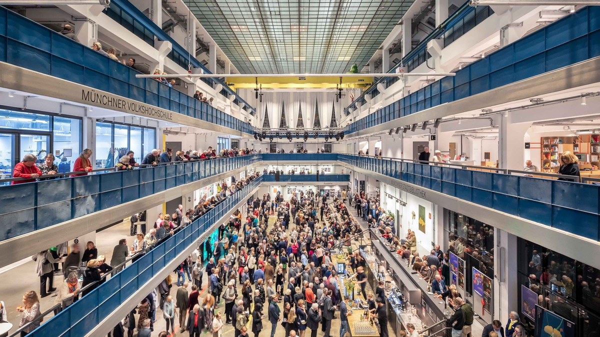Blick von oben auf Halle E, seitlich die blauen Geländer der Stockwerke zu sehen, im Erdgeschoss befinden sich viele Menschen