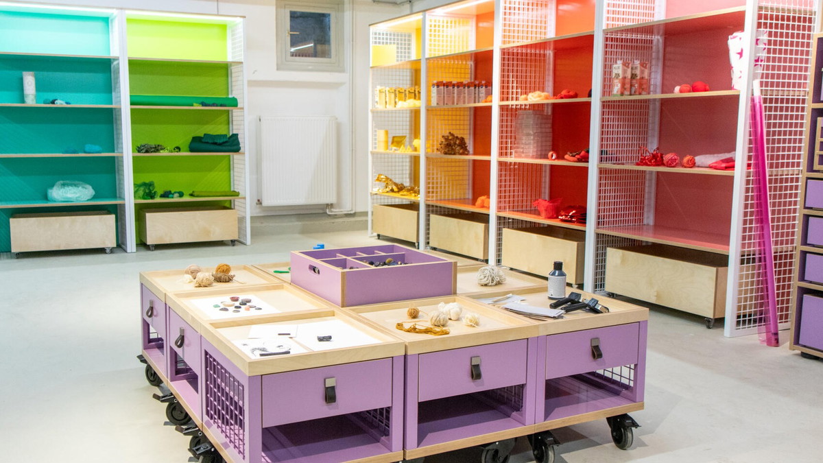 Raum mit Regalen in verschiedenen Farben an den Wänden. Materialien farblich zugeordnet. Rollbare Materialwagen in der Mitte.