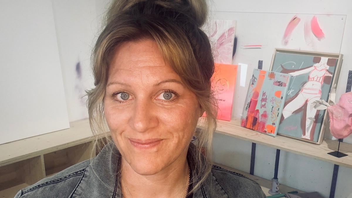 Nicole, mittelblonde Haare, Blaue Augen, Bun auf dem Kopf mit Pony. Bilder Skizzen unscharf im Hintergrund.