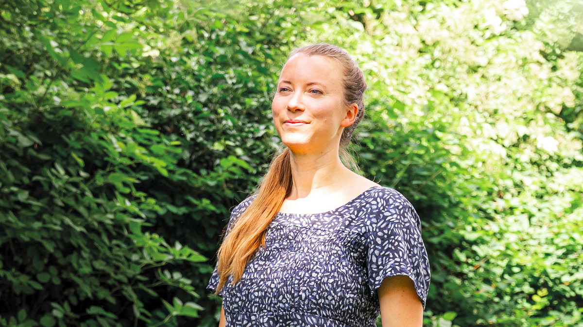 Lächelnde Frau vor grüner Hecke, die von der Sonne angestrahlt wird.