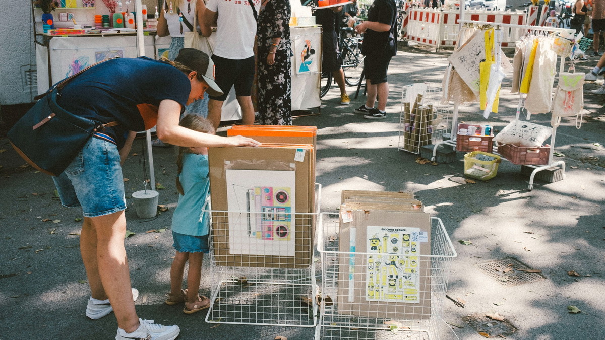 Ein Erwachsener und ein Kind betrachten Kunstdrucke an einem Stand beim Büdchentag am Friedensplätzchen.